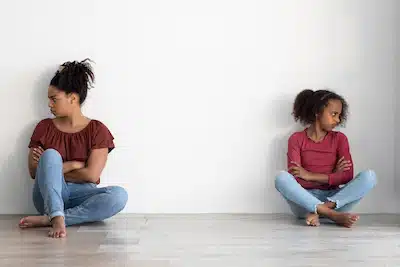 a mother and daughter sitting on the floor, turned away from each other