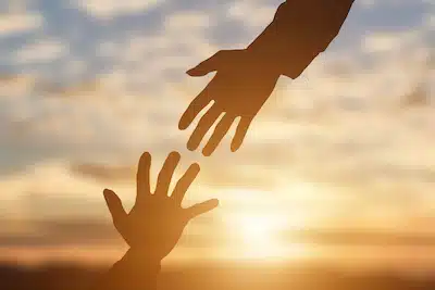 two hands reach for each other with the sunset in the background