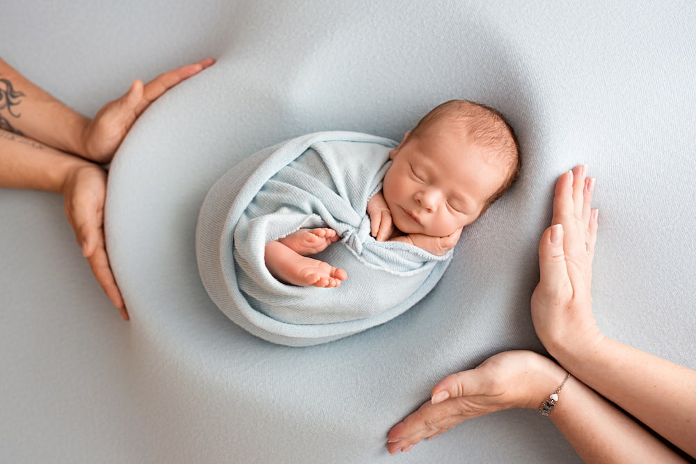 newborn baby wrapped in blue, cradled by two hands