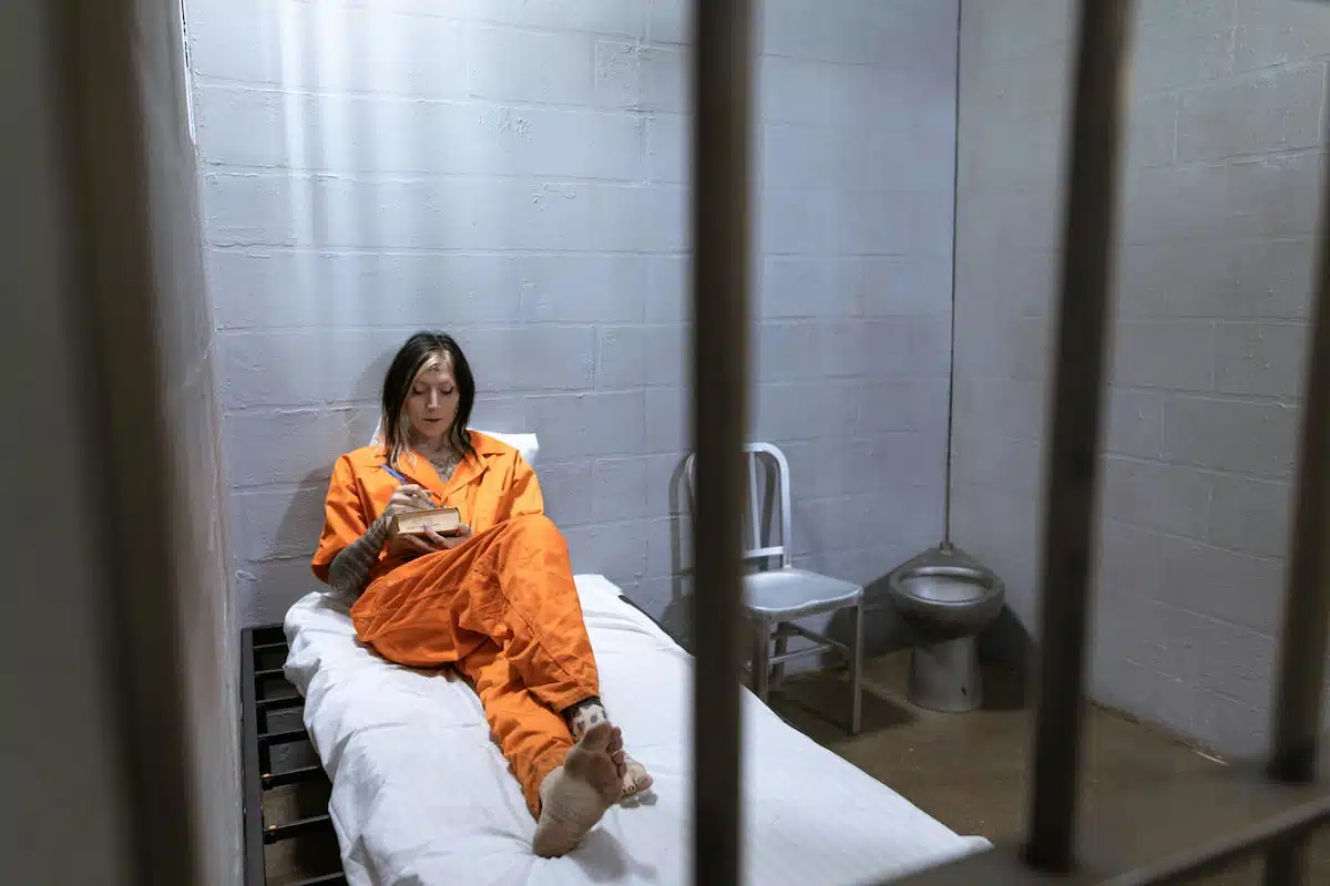 Woman in Orange Overalls Sitting on Bed with White Linens